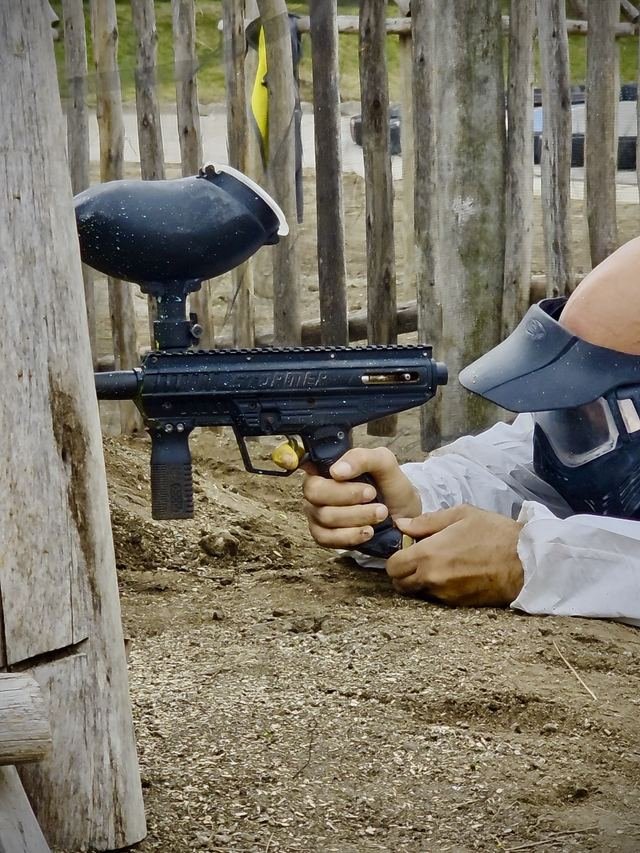 Manos apuntando la marcadora de paintball desde la barricada